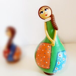 Μια νεροκολοκύθα μεταμορφώνεται σε κούκλα! Μια νεροκολοκύθα έμεινε πολλές ώρες κάτω από τον ήλιο για να στεγνώσει. Δυο χέρια έπλασαν το κεφάλι, τη μύτη, τα μάτια, τα χέρια και τα στολίδια της και τα πρόσθεσε πάνω στη νεροκολοκύθα και της έβαλε μια βάση για να στέκεται όρθια και καμαρωτή πάνω στο ράφι, στο τραπέζι, στο τζάκι, στη βιτρίνα και όπου αλλού μπορείς να σκεφτείς! Το μόνο που κάνει είναι να σε μαγεύει με την παρουσία της και να διακοσμεί με τον δικό της μοναδικό τρόπο το χώρο σου! Μια νεροκολοκύθα έργο τέχνης, ζωγραφισμένη όλη στο χέρι σε πολλά χρώματα και σχέδια για να διαλέξεις εκείνη που σου αρέσει το περισσότερο! Αν την κουνήσεις ακούς και τα σπόρια της! Κι αν την παρατηρήσεις όλο και κάτι έχει να σου πει με το σκέρτσο και τα μάτια της!